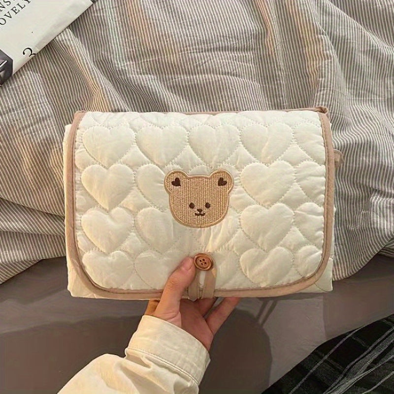 Portable changing mat with cream bear pattern, foldable, breathable polyester, adjustable strap, ideal for short trips.