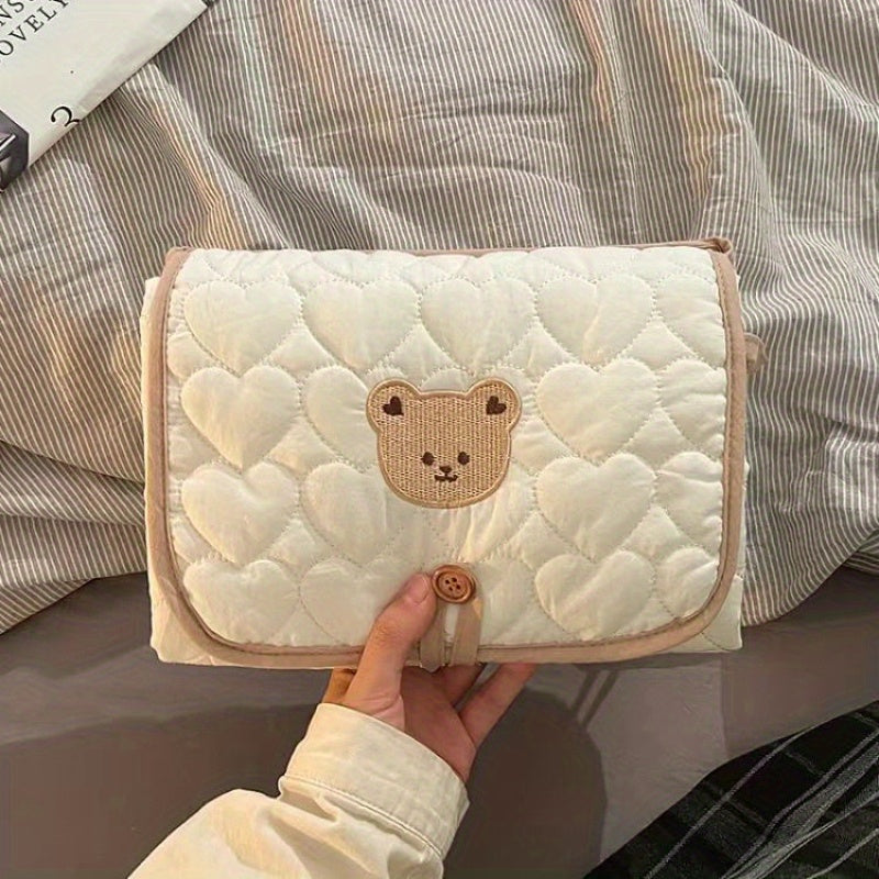 Portable changing mat with cream bear pattern, foldable, breathable polyester, adjustable strap, ideal for short trips.